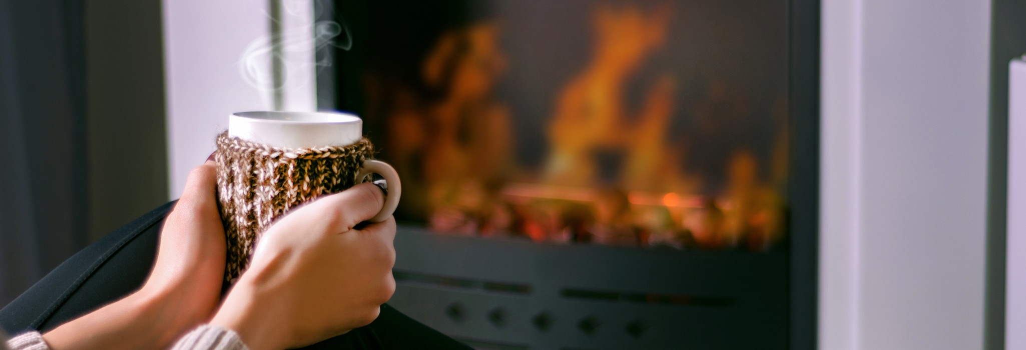 Young girl sitting in front of the fireplace and holding warm drink in hand.