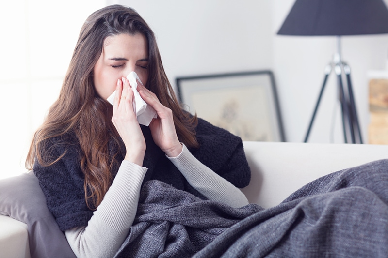 Blog Title: What Does Indoor Air Quality Have to Do With Allergies? Photo: Woman sneezing nose with tissue