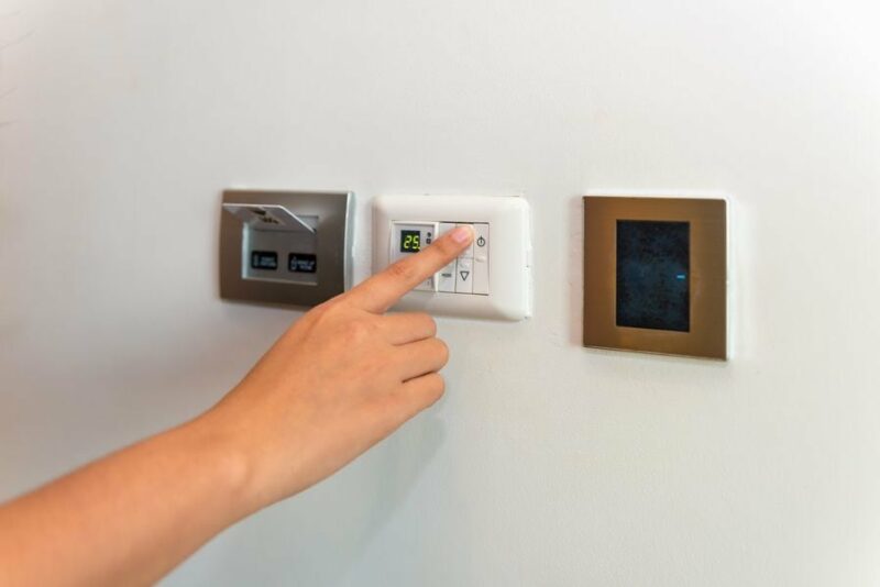 Image of someone pressing on a control panel attached to an HVAC unit. Heat Pump Versus Furnace.