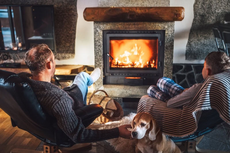 Father with son sitting in comfortable armchairs in their cozy country house near fireplace and enjoying a warm atmosphere.